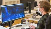 Ein junger Mann, der Medieninformatik studiert hat, sitzt am Schreibtisch vor zwei Monitoren und arbeitet an der Modellierung.