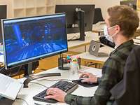 Ein junger Mann, der Medieninformatik studiert hat, sitzt am Schreibtisch vor zwei Monitoren und arbeitet an der Modellierung.