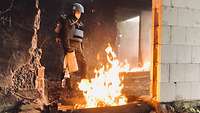 Ein Blauhelm-Soldat steht im Erdgeschoss eines Hauses und löscht ein Feuer.