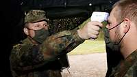 Ein Soldat misst bei einem anderen Soldaten an der Stirn Fieber