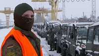 Ein Soldat mit Warnweste steht am Gleis. Im Hintergrund stehen Fahrzeuge auf Waggons 