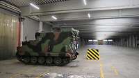 In einer leeren Wellblechhalle steht ein kleiner Panzer.