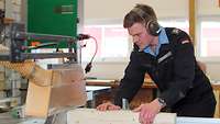 Demuth an der Sägemaschine Ein uniformierter Marinesoldat sägt Holz an einer Maschine.