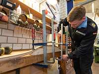 Demuth passt Holz einer runden Oberfläche an Ein Soldat in Marineuniform arbeitet an einer Werkbank mit Holz.