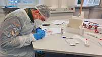 Ein Soldat in medizinischem Vollschutz untersucht einen Schnelltest.