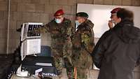 Soldaten und ein Zivilist stehen in einem Raum vor aufgestellten Bildschirmen.