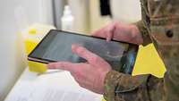Ein Soldat fotografiert mit einem Tablet einen Impfzettel, um diesen zu digitalisieren