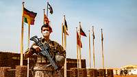 Ein Soldat steht im Eingangsbereich des Camps Castor. Hinter ihm wehen die Nationalflaggen an Masten 