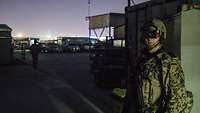 Ein Soldat mit Waffe, Schutzweste, Helm und Nachtsichtbrille steht vor einem Container bei Dunkelheit
