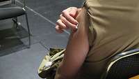 Zwei Finger halten einen Tupfer an den linken Oberarm