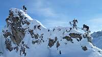 Auf einem schneebedeckten Gebirgsgrat klettern vier Soldaten in schneegetarnten Kletteranzügen.