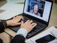 Drohnen-Debatte 2020 Eine Person tippt auf die Tastatur eines Laptops, auf dem Bildschirm ist das Gesicht eines Mannes zu sehen