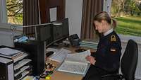 Eine junge Frau in dunkelblauer Marineuniform sitzt an einem Schreibtisch und blättert durch Notenblätter.