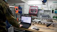 Ein Soldat bedient einen Laptop vor einer Maschine in einer Werkstatt
