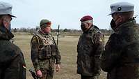 Auf einer verödeten Wiese stehen vier Soldaten in Flecktarnuniform und unterhalten sich. Drei tragen Mund-Nasen-Bedeckung.