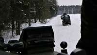 Vor dem Bergepanzer steht ein Geländefahrzeug und weiterer Panzer am Straßenrand