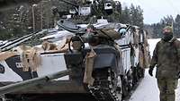 Zwei Soldaten stehen neben einem Schützenpanzer und unterhalten sich