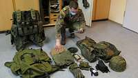 Ein Soldat in Uniform prüft in einem Zimmer seine persönlich Ausrüstung gemäß einer Liste.