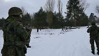 Fünf Soldaten bewegen sich versetzt über eine Straße und suchen diese nach gefährlichen Gegenständen ab.