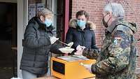 Zwei Frauen geben eine Suppe an einen Soldaten aus