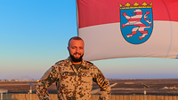 Ein Soldat steht vor der hessischen Flagge, hinter ihm die jordanische Wüste