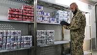 Ein Soldat hält ein Klemmbrett in der Hand und überprüft die vorhandene Ware im Kühlcontainer
