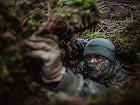 Ein Soldat befindet sich gut getarnt im Versteck. Nur sein oberes Gesichtsfeld macht ihn erkennbar.