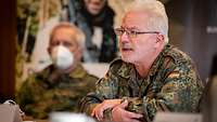 Ein älterer Soldat sitzt an einem Tagungstisch und redet.