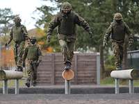 Drei Soldaten überqueren jeweils individuell einen Baumstamm.