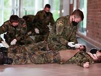Soldaten üben in einem Raum Abläufe der Ersten Hilfe untereinander.