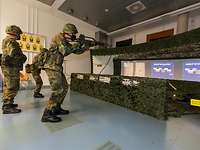 Soldaten stehen in einem Raum und simulieren Schüße auf einem riesigen Computerbildschirm.