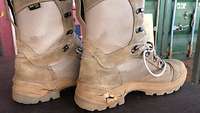 Ein Paar Stiefel mit defekter Sohle steht auf dem Tisch