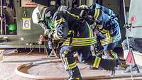 Zwei Soldaten in Schutzanzügen laufen mit einem Feuerwehrschlauch in einer Halle vor