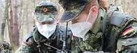 Zwei Soldaten mit Mund- und Nasenschutzmaske liegen im Gelände und besprechen sich
