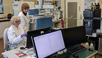 Forscherinnen an Computern und Analysegeräten im WIS Eine Frau sitzt an einem Schreibtisch mit einem Computer, im Hintergrund steht eine weitere Frau in einem weißen Kittel.
