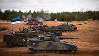 Multinationalität Mehrere Panzer mit unterschiedlichen Länderflaggen auf einem Übungsplatz.