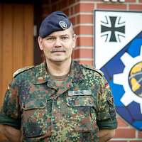 Frontale Portraitaufnahem des Herrn Oberstleutnant Brune vor dem Wappen seiner Dienststelle.