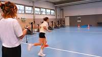 Frau rennt in der Turnhalle um Pylone 