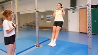 Frau hängt in der Turnhalle an einer Klimmzugstange 