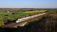 ICE mit grünen Streifen fährt auf einer Bahntrasse durch die Landschaft.