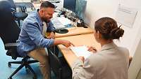 Frau sitzt bei einem Mann im Büro und füllt Unterlagen aus