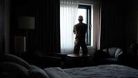 Ein Soldat steht in einem Raum vor einem Fenster und blickt nach draußen