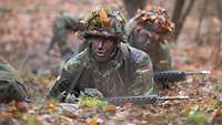 Soldaten gleiten mit dem Gewehr G36 über den Waldboden.