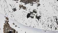 Ein Hubschrauber schwebt über einem schneeweißen Gebirgshang.
