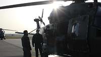 Drei Soldaten stehen im Gegenlicht neben einem Hubschrauber auf dem Landeplatz.