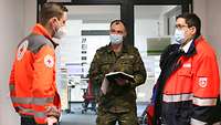 Ein Soldat und zwei DRK-Mitarbeiter in Rettungsjacken vor dem Eingang des Lagezentrums