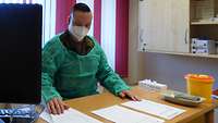 Soldat sitzt in Schutzkleidung an einem Schreibtisch.