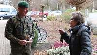 Ein freundlich blickender Soldat in Flecktarnuniform und eine ältere Dame unterhalten sich im Freien.