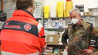 Ein Generalarzt steht vor einem Regal im Materiallager und spricht zu einem Vertreter der Johanniter