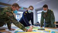 Zwei Soldaten und eine Soldatin stehen an einem Tisch auf dem eine Lagekarte liegt. Alle tragen Mund- Nasenschutz